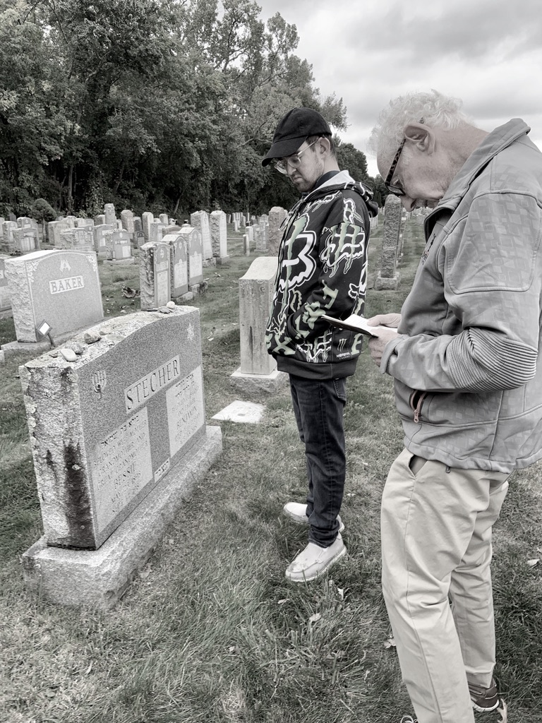 two men standing next to a gravestone with the last name Stecher